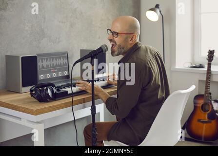 Musicien chantant et jouant de la musique sur un clavier MIDI dans son studio d'enregistrement à domicile Banque D'Images