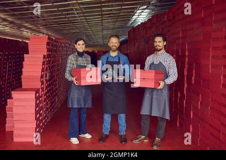 Équipe de travailleurs heureux de l'usine de chaussures debout dans l'entrepôt et montrant la nouvelle chaussure en cuir Banque D'Images