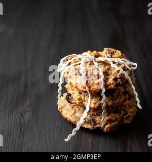 Biscuits maison aux raisins secs de gruau, noués avec une tresse blanche sur un fond en bois noir Banque D'Images