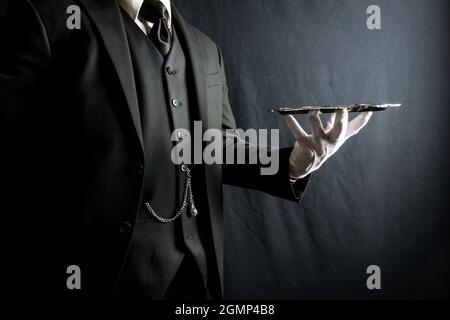 Portrait de Butler ou de garçon en costume sombre et gants blancs tenant un plateau de service argenté sur fond noir. Concept de l'industrie des services. Banque D'Images