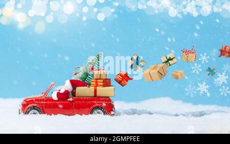 Le Père Noël en voiture rouge livre des cadeaux de noël ou du nouvel an sur fond neigeux. Banque D'Images