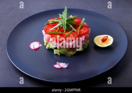 Tartare de thon frais avec avocat, arugula, tomates cerises, radis, piment et lime. Hors-d'œuvre froid traditionnel de la cuisine française. Gros plan/ Banque D'Images