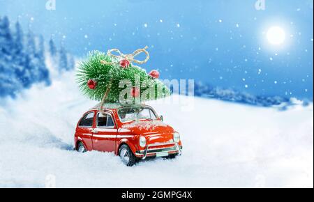 Voiture rouge rétro transportant l'arbre de noël sur le toit dans la forêt enneigée d'hiver. Arrière-plan de Noël. Carte de vacances. Copier l'espace. Banque D'Images