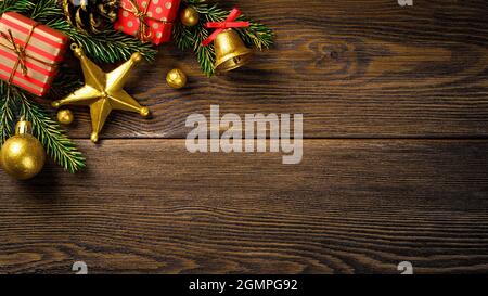 Coin de Noël avec branches de sapin pinède cône cloche et boîtes-cadeaux rouges sur panneau rustique brun. Banque D'Images