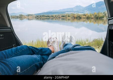 Deux paires de jeans portant des jambes dans des sneakers blanches. Couple se détendant dans le coffre de campeur et appréciant la montagne automnal vue sur le lac. Un couple chaleureux au début de l'automne Banque D'Images