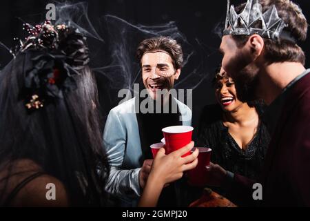 joyeux amis interraciaux dans halloween maquillage toaster avec des tasses en plastique sur noir Banque D'Images