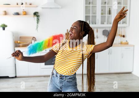 Femme afro-américaine émotive s'amusant tout en nettoyant à la cuisine Banque D'Images