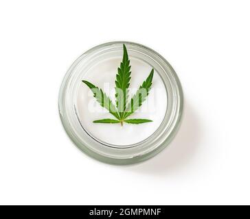 Crème hydratante pour les soins de la peau et feuille de cannabis sativa verte dans un pot en verre isolé sur fond blanc. Concept de cosmétiques de chanvre. Marijuana médicale. Banque D'Images