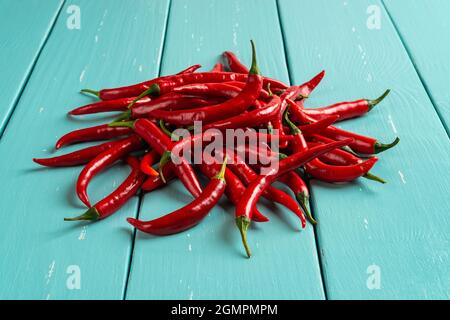 Tas de piments rouges chauds sur une table en bois turquoise. Gros plan sur les gousses épicées de piment. Piments forts frais entiers pour la cuisine. Banque D'Images