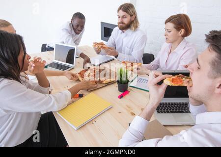 Joyeux collègues divers s'amusent à la pause déjeuner au bureau, souriant employés multiraciaux rire et parler de manger de la pizza Banque D'Images