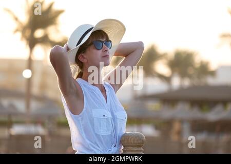 Jeune femme touriste dans des vêtements décontractés appréciant la chaude soirée ensoleillée sur le bord de mer. Vacances d'été et concept de voyage. Banque D'Images