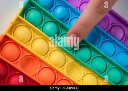 Doigt poussant un point d'un jouet coloré pour enfants sur une table blanche Banque D'Images