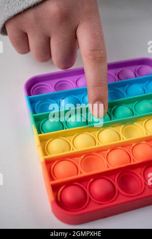 Doigt poussant un point d'un jouet coloré pour enfants sur une table blanche Banque D'Images