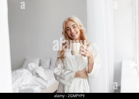 Bonne jeune femme du millénaire jolie femme caucasienne en peignoir aime le matin et boire un délicieux café frais Banque D'Images