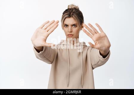 Portrait d'une femme adulte qui s'étire les mains pour arrêter, dire non, refusant quelque chose avec l'expression du visage frognant, se tenant sur fond blanc Banque D'Images