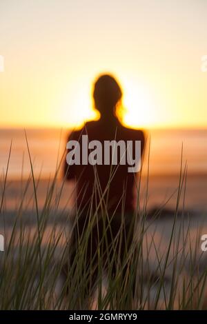 Un homme debout seul sur une plage qui donne sur la mer et le soleil couchant, plage Heaphy, parc national de Kahurangi Banque D'Images