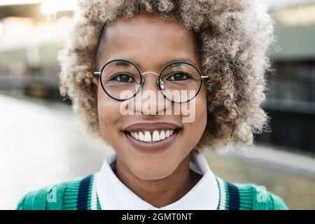 Portrait d'une jeune fille africaine souriant sur l'appareil photo en plein air dans la ville - Focus sur le visage Banque D'Images