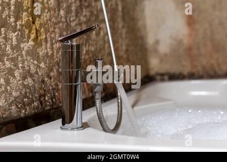 Jacuzzi, eau courante d'un robinet et un jacuzzi de remplissage, une eau mousseuse, des murs en pierre naturelle et une salle de bains d'époque Banque D'Images