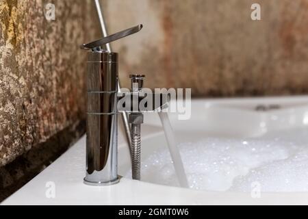 Jacuzzi, eau courante d'un robinet et un jacuzzi de remplissage, une eau mousseuse, des murs en pierre naturelle et une salle de bains d'époque Banque D'Images