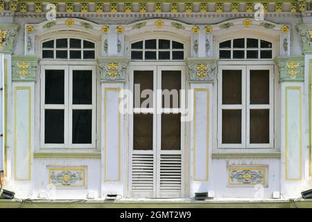 Extérieur du magasin Peranakan chinois du détroit de Singapour avec fenêtres voûtées, volets à persiennes en bois blanc, colonnes ornées avec finitions vertes jaunes Banque D'Images