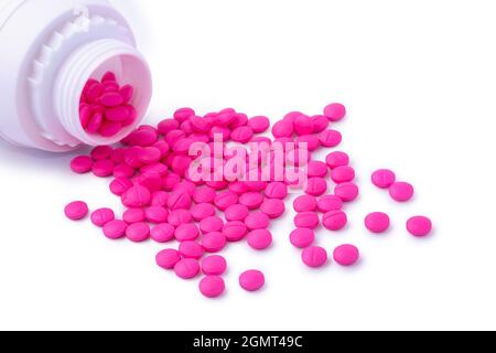 pilules ou comprimés qui se répandent hors de la bouteille de pilules en plastique, couleur rose vif médicaments isolés sur fond blanc, vue rapprochée Banque D'Images