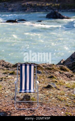 Chaises pliantes sur la rive d'une rivière de montagne par une belle journée chaude. Un endroit calme et calme pour se détendre et réfléchir. L'équipement et le repos d'un touriste. Banque D'Images