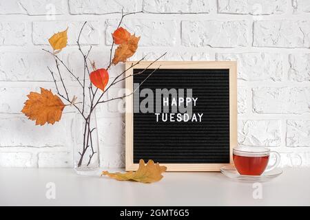 Happy Tuesday texte sur tableau noir de lettres et bouquet de branches avec feuilles jaunes sur clotespins dans vase sur table modèle pour carte postale, salutation ca Banque D'Images