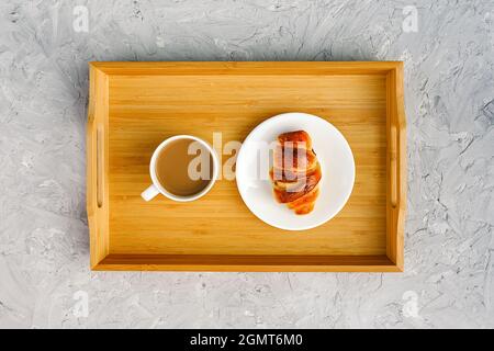 Tasse de café avec lait et croissant fraîchement cuit sur plateau en bois sur table en pierre grise. Concept Good Morning Top vue. Banque D'Images