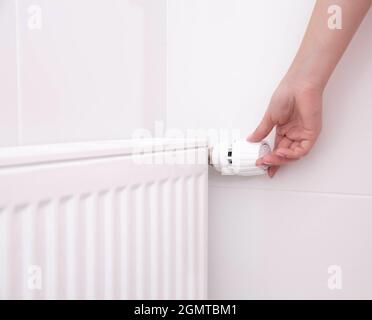 La main d'une femme tient la poignée du thermostat de chauffage. Concept de coût du service de chauffage, augmentation du prix du service public Banque D'Images