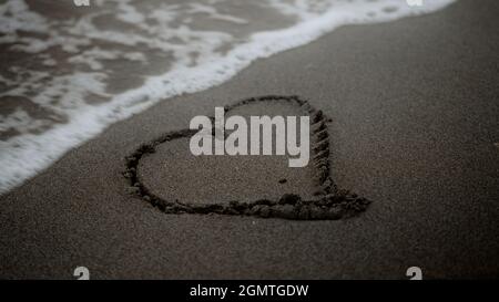 Le symbole du coeur dessiné sur une plage, vague de mer l'effacer, métaphore de l'amour et de la séparation Banque D'Images