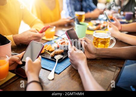 Groupe de jeunes gens connectés utilisant le téléphone portable au bar de la terrasse Banque D'Images