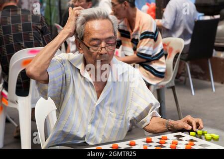 Chinatown, Singapour - 1er avril 2011 l'homme fumeur s'est concentré sur son jeu de dames dans cette place ouverte et bruyante du centre de Chinatown à Singapour Banque D'Images