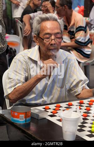 Chinatown, Singapour - 1er avril 2011 l'homme fumeur s'est concentré sur son jeu de dames dans cette place ouverte et bruyante du centre de Chinatown à Singapour. Banque D'Images