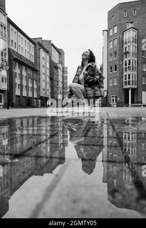 fille près de la flaque d'automne avec des réflexions sur la place de la ville, monochrome Banque D'Images