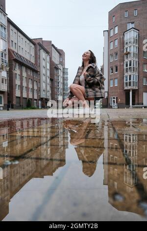 fille près de la flaque d'automne avec des réflexions sur la place de la ville Banque D'Images