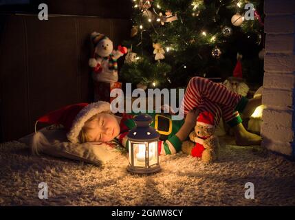 Mignon petit enfant, un garçon habillé de pyjama elf et un chapeau de père Noël, dormant dans un pouf doux sous un arbre de Noël décoré. En attendant un miracle, un fa Banque D'Images