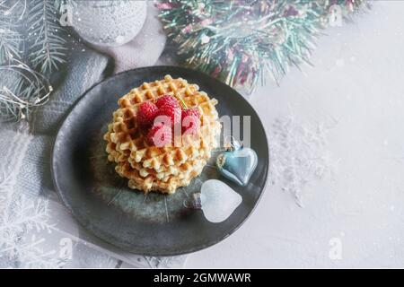 Gaufres rondes avec framboises sur la table de Noël. Pâtisseries festives sur le fond d'un arbre de Noël Banque D'Images