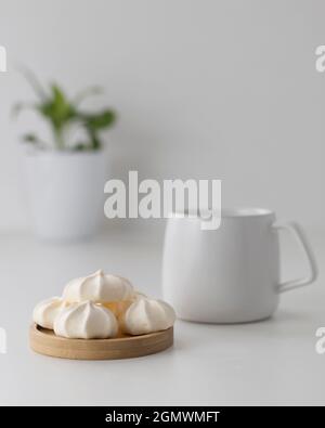 crème meringues dans une assiette en bois avec une tasse sur fond blanc Banque D'Images