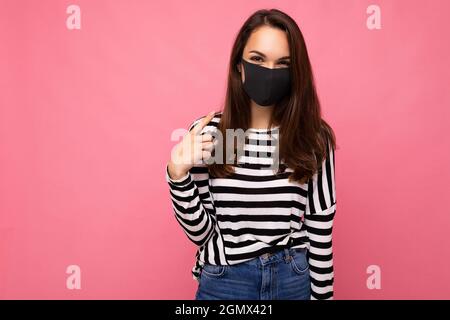 Jeune femme portant un masque anti-virus pour prévenir D'autres de l'infection corona COVID-19 et du cov 2 du SRAS ont été isolés sur fond rose Banque D'Images