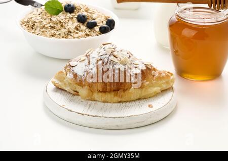 croissant cuit arrosé de sucre en poudre, flocons d'avoine dans une assiette en céramique sur une table blanche, petit déjeuner Banque D'Images