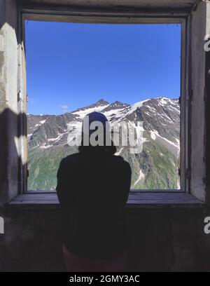 Une femme regarde par la fenêtre d'une maison détruite. Paysage de montagne depuis la fenêtre d'une vieille maison. Mise au point en arrière-plan. Banque D'Images