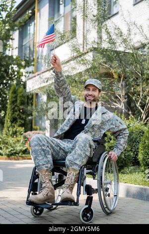 soldat gai avec petit drapeau américain dans la main levée regardant la caméra à l'extérieur Banque D'Images