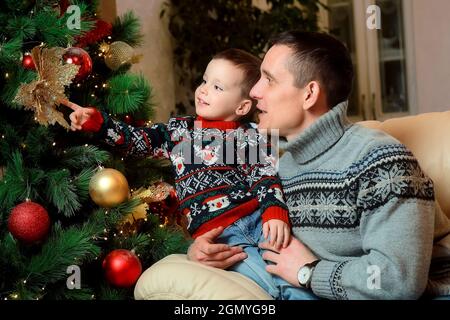 Portrait d'un père avec un jeune fils près d'un arbre de Noël avec des jouets de Noël. Garçon et père regardent les boules de Noël sur l'arbre de Noël. Banque D'Images