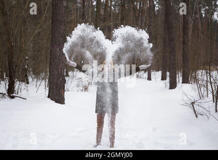 une jeune femme méconnaissable vêtue de vêtements chauds a du plaisir à jouer à l'extérieur en hiver. Elle jette de la neige avec les mains, qui scinde en forme de coeur. Amour Banque D'Images