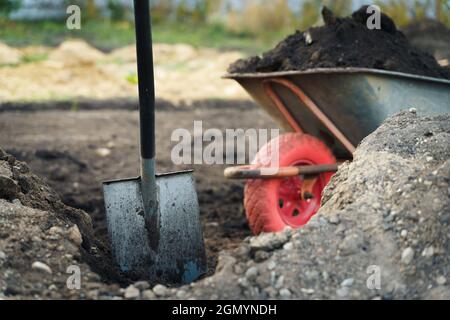 Travailler avec des outils de jardin, une pelle et une brouette sur le site d'une maison de campagne. Préparation aux travaux de construction. Banque D'Images