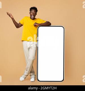 Surprise jeune Noir Guy debout à côté de grand smartphone avec écran blanc Banque D'Images