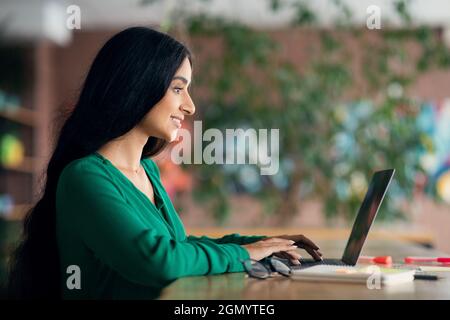 Vue latérale d'une femme brunette aux cheveux longs utilisant un ordinateur portable, intérieur de café Banque D'Images