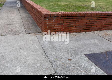 Mur de soutènement de briques rouges bas séparant une zone herbeuse des trottoirs, vue d'angle à une intersection, aspect horizontal Banque D'Images