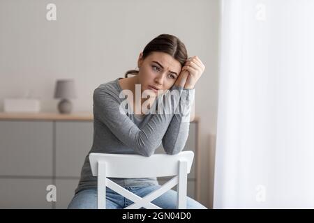 La jeune femme bouleversée s'assoit seule, regardant loin avec une triste expression à l'intérieur de la maison Banque D'Images