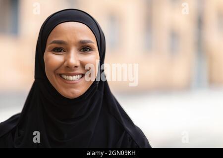 Portrait d'une jeune femme musulmane souriante en hijab noir debout à l'extérieur Banque D'Images
